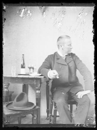 Gustav Vigeland sitter ved et bord med flaske og to glass